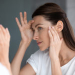 Satisfied woman looking in mirror check face after beauty treatment