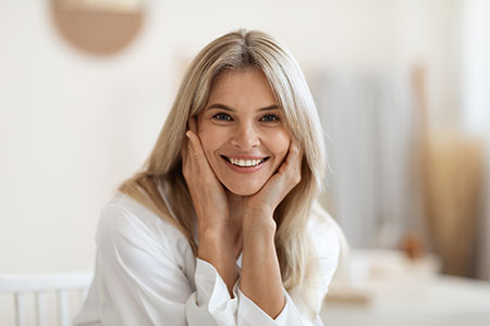 Beautiful blonde middle aged woman smiling at camera, touching her face