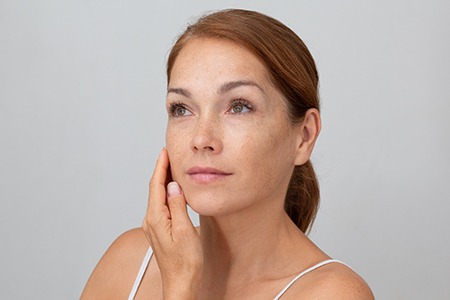 Woman holding fingers on cheek with closed eyes showing soft skin