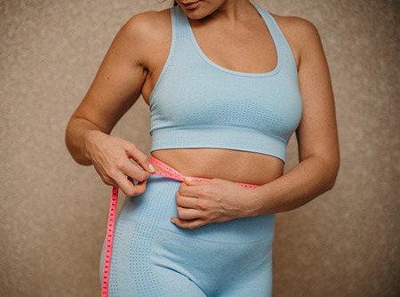 slim woman measuring waist with tape measure at home